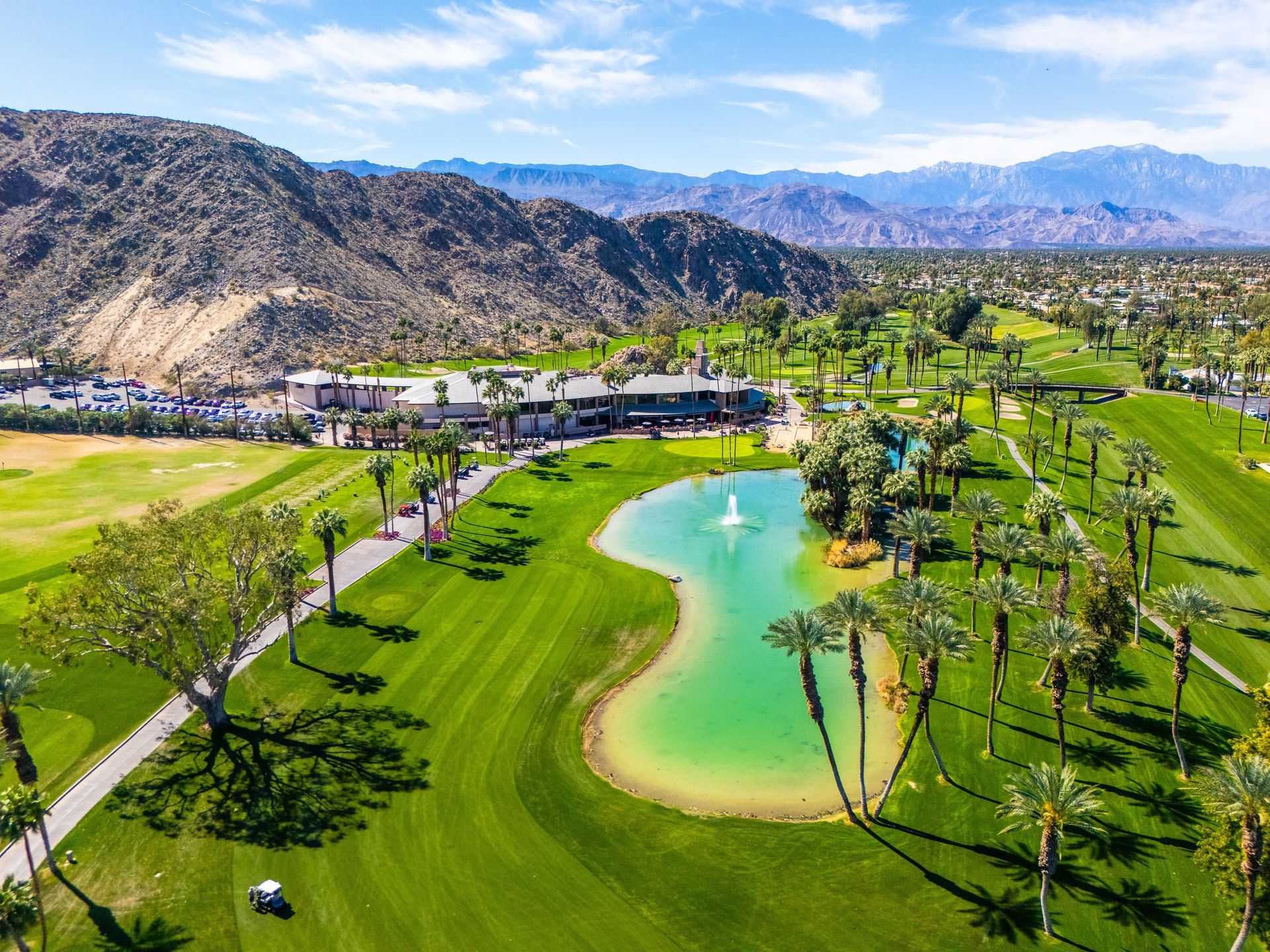 Desert-modern home at 77013 Desi Dr, Indian Wells — photographed for The Chavez Team at The Agency — aerial over the golf course, lake and mountains