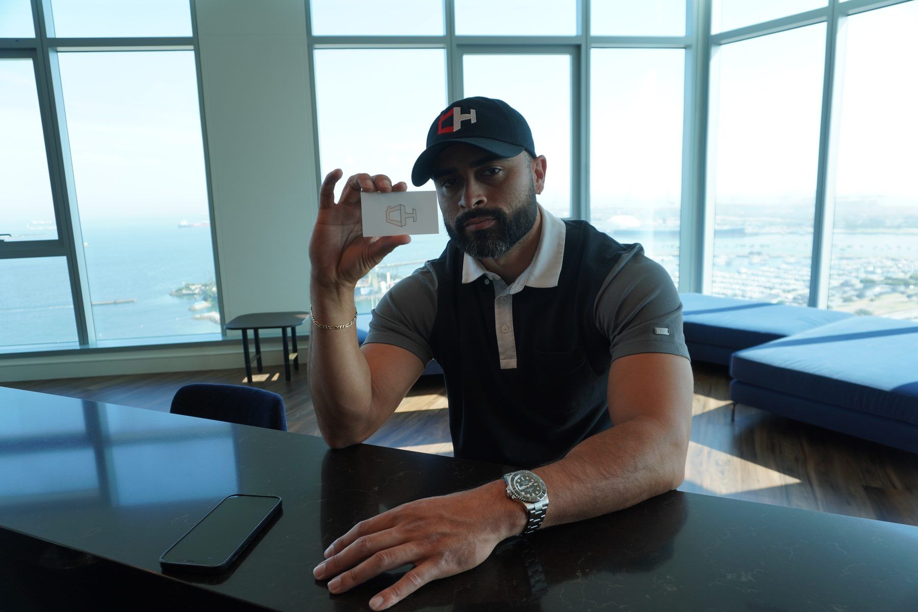 Ismael Chavez at a window desk holding his business card, Long Beach harbor behind him